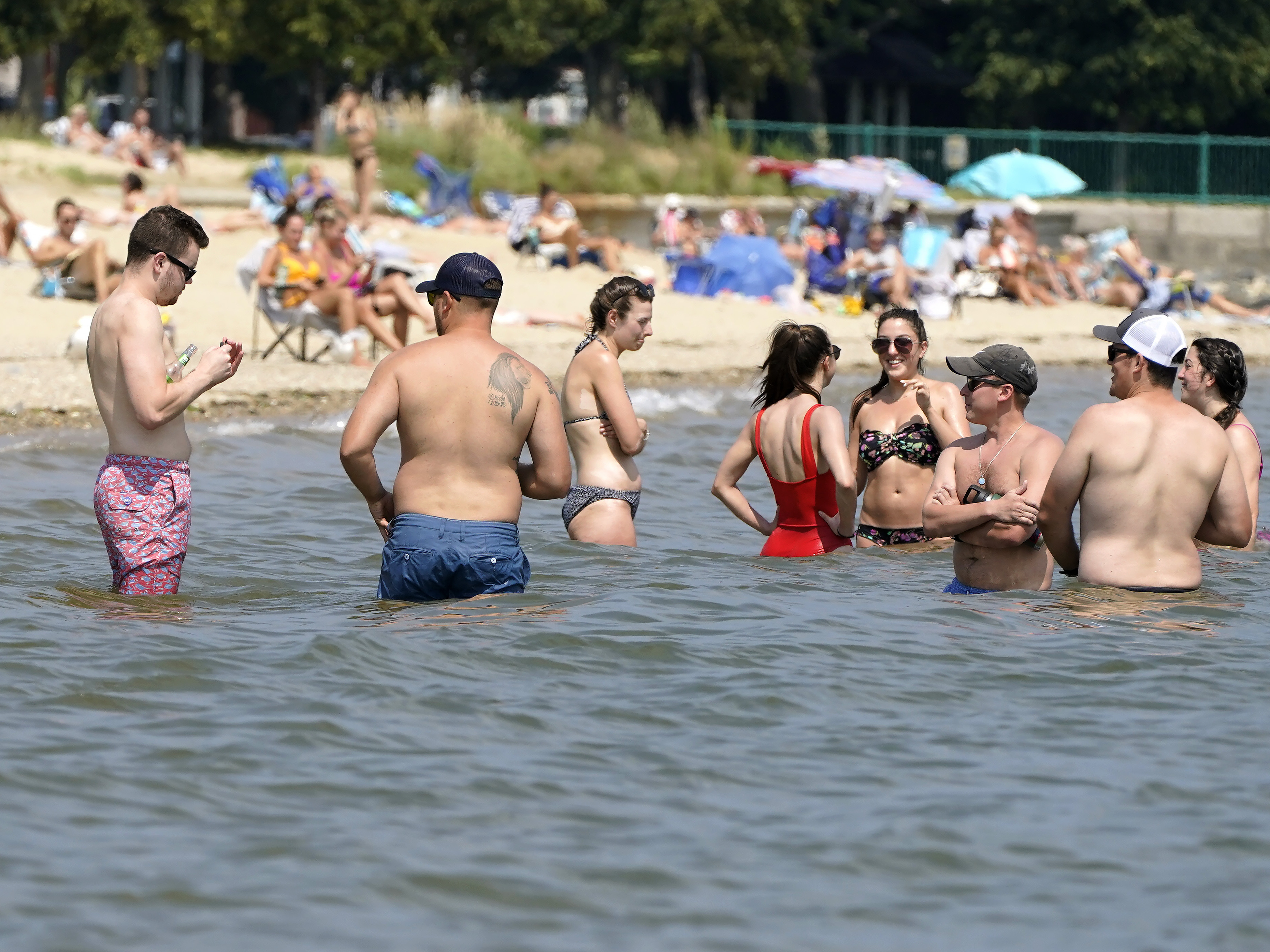 caption: Beachgoers stand in the water of Dorchester Bay to cool off, in the South Boston neighborhood of Boston, Wednesday, Aug. 11, 2021.