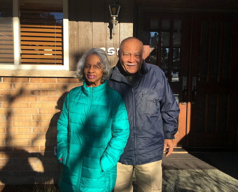 caption: Violet and Norward Brooks in front of a house they struggled to buy due to discrimination.