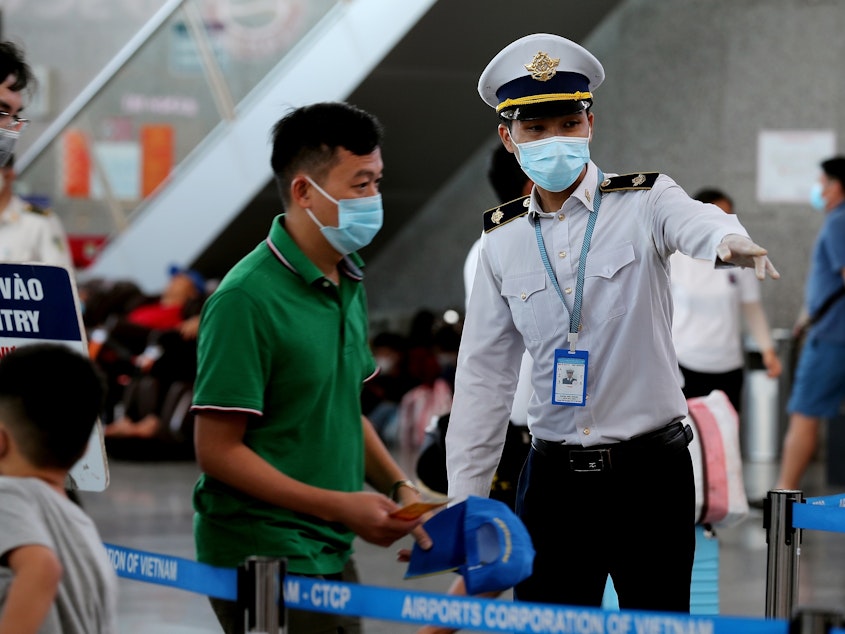 caption: A staff member from Vietnam's disease control authority assists passengers as they queue up for temperature checks at the departure terminal at Da Nang's international airport on Monday.