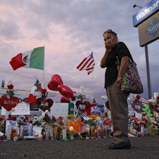 caption: Catalina Saenz wipes tears from her face as she visits a makeshift memorial near the scene of a mass shooting at a shopping complex in El Paso, Texas. A list of the people who died in the weekend shooting rampage at the Walmart, shows that most of the victims had Latino surnames and included one German national.