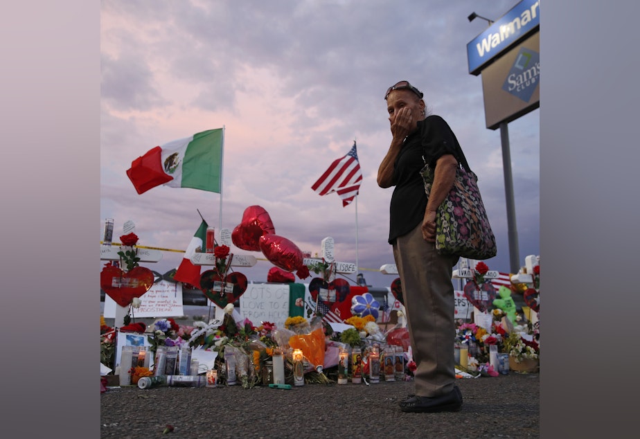 caption: Catalina Saenz wipes tears from her face as she visits a makeshift memorial near the scene of a mass shooting at a shopping complex in El Paso, Texas. A list of the people who died in the weekend shooting rampage at the Walmart, shows that most of the victims had Latino surnames and included one German national.