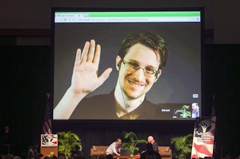 caption: Edward Snowden appears on a live video feed broadcast from Moscow at an event sponsored by the ACLU Hawaii in Honolulu on Feb. 14, 2015.