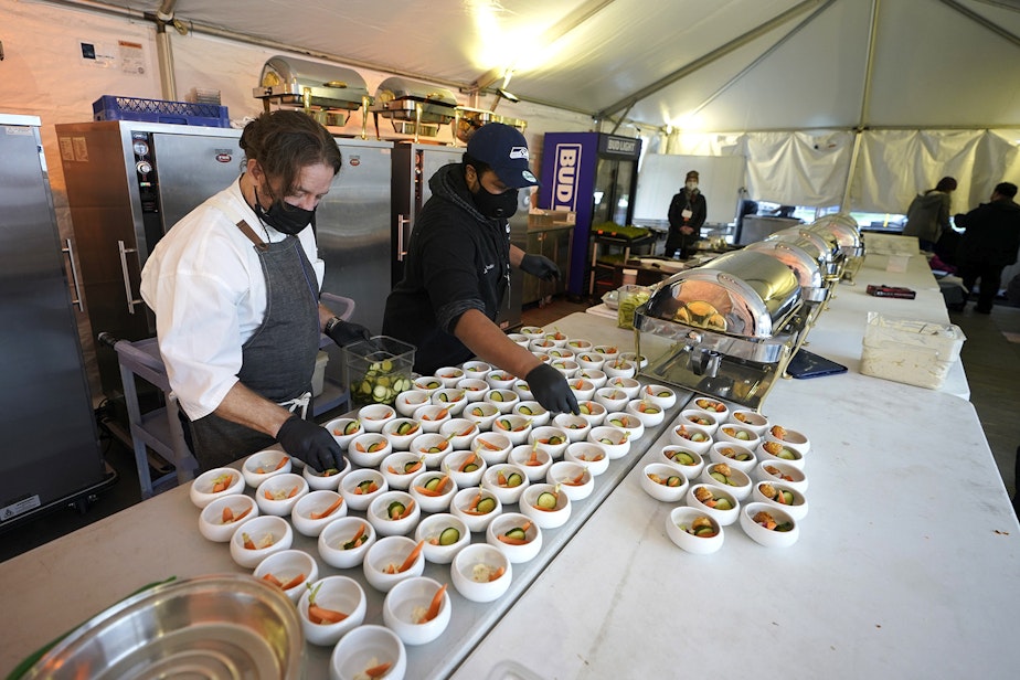 caption: Jason Wilson, left, a chef at The Lakehouse, a restaurant located in Bellevue, Wash., and sous chef Demetrius Parker, right, prepare dishes for the first course of a meal for diners in an outdoor tent set up on the turf at Lumen Field, Thursday, Feb. 18, 2021, in Seattle. Wilson and Parker were two of the chefs taking part in the inaugural night of the "Field To Table" event at stadium, which is home to the Seattle Seahawks NFL football team. 