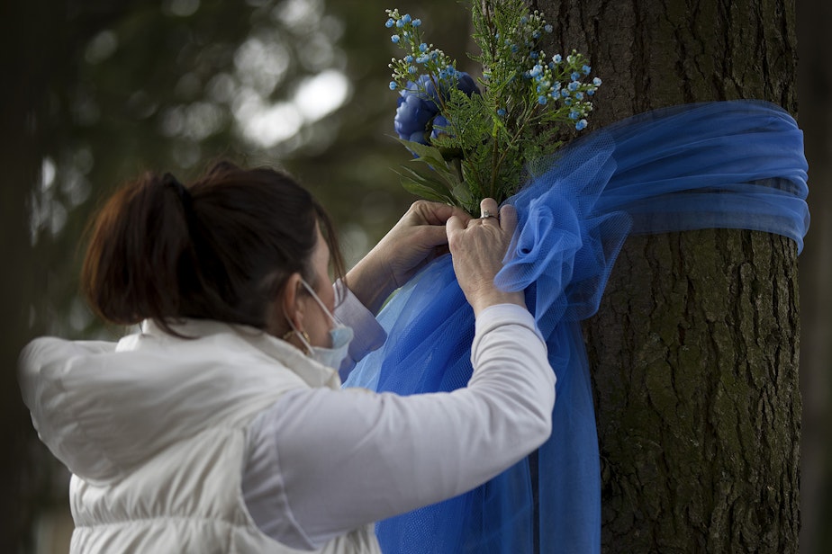 caption: Tricia LaVoice, of Kirkland, ties blue ribbons and flowers to trees outside of the Life Care Center of Kirkland, the long-term care facility at the epicenter of the coronavirus outbreak in Washington state, on Wednesday, March 11, 2020, in Kirkland. "Just trying to show them that the community cares," LaVoice said. "Love really is a big part of healing."