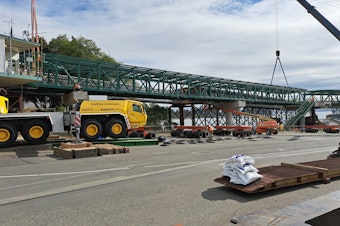 caption: Construction crews lower two new bridge spans onto concrete pillars, creating a new overhead walkway for the ferry terminal at Bainbridge Island, August 12, 2023.