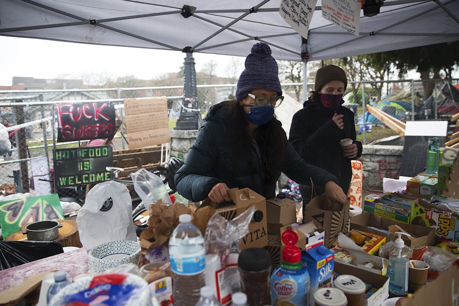 caption: Community members D, left, and A, right, give out food and coffee while working in an area set up for mutual aid to help those in need of support on Wednesday, December 16, 2020, at Cal Anderson Park in Seattle.