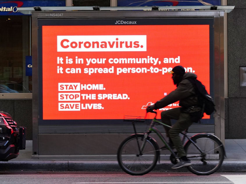 caption: A person on a bike rides by a sign in New York City urging people to stay home in May. As the pandemic drags on, some workers are facing tough choices — balancing potential risks of unwittingly spreading the disease against the possibility of losing pay during a quarantine.