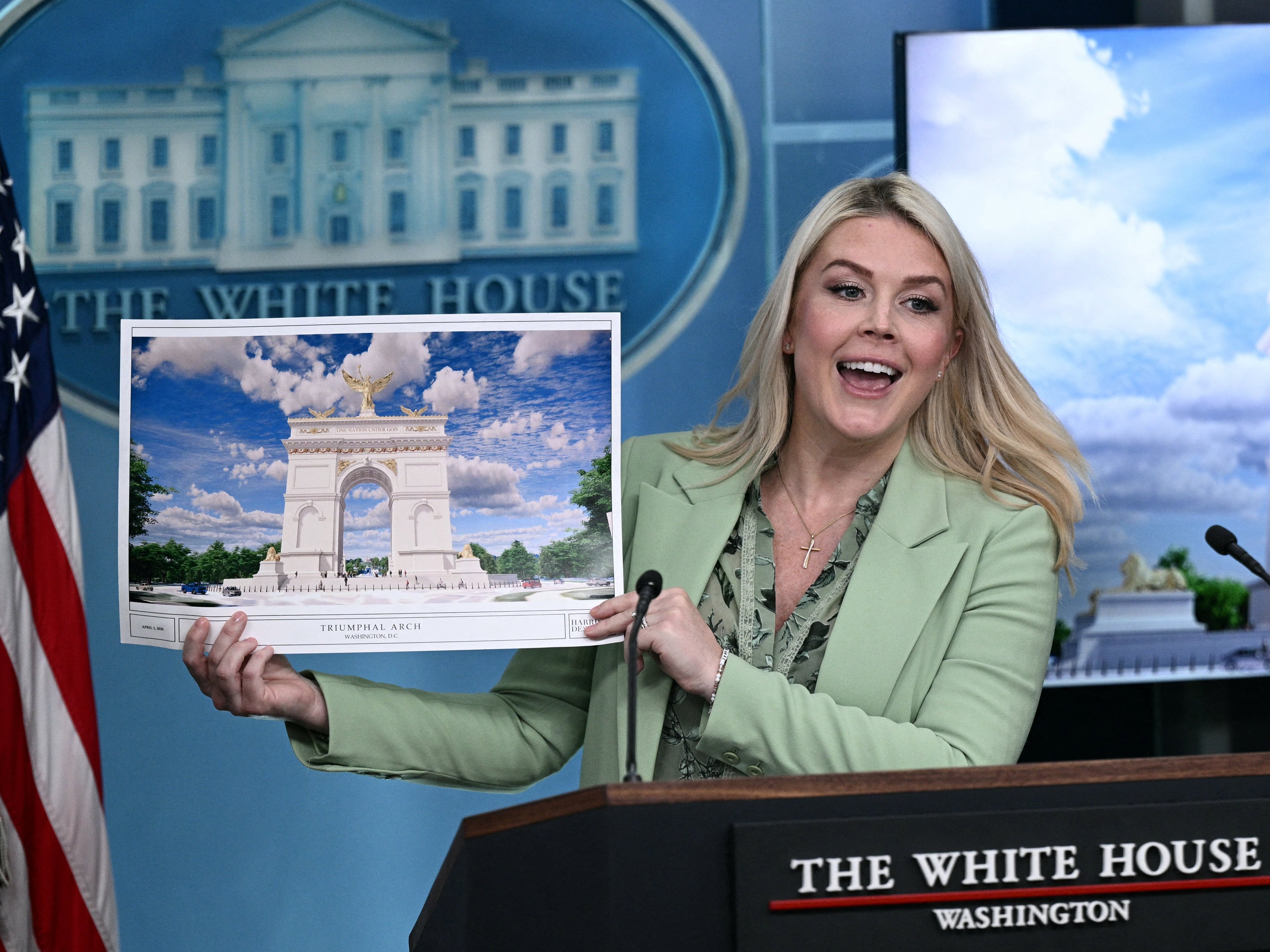 caption: White House press secretary Karoline Leavitt shows a rendering of the planned triumphal arch to be added to Washington, D.C.'s National Mall at a meeting on Wednesday.