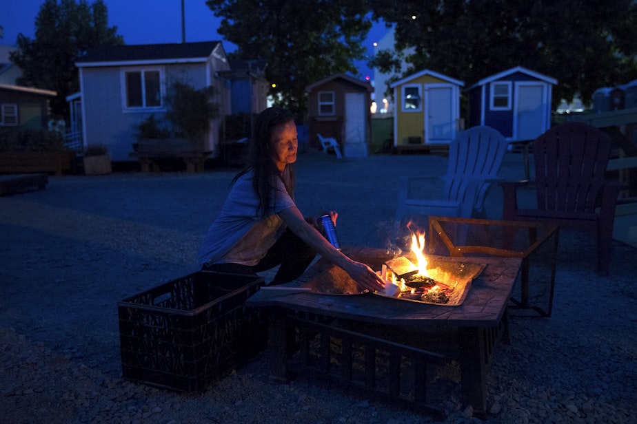 caption: Rebecca adds wood to a fire on Sunday, June 9, 2019, at the Georgetown tiny house village in Seattle. 