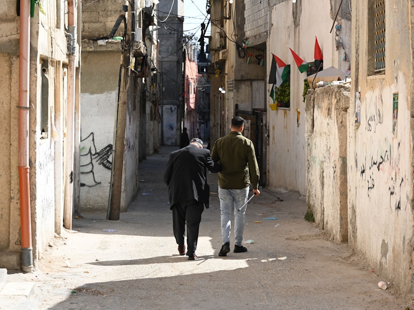 caption: People walk down the narrow streets of the Al-Am'ari refugee camp in Ramallah in the West Bank on Oct. 31, 2023.