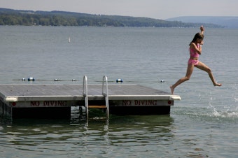 caption: A young swimmer jumps into Skaneateles Lake in Skaneateles, N.Y. The small lakeside town in upstate New York's Finger Lakes is just one of many destinations you could consider visiting this summer. (Kevin Rivoli/AP)