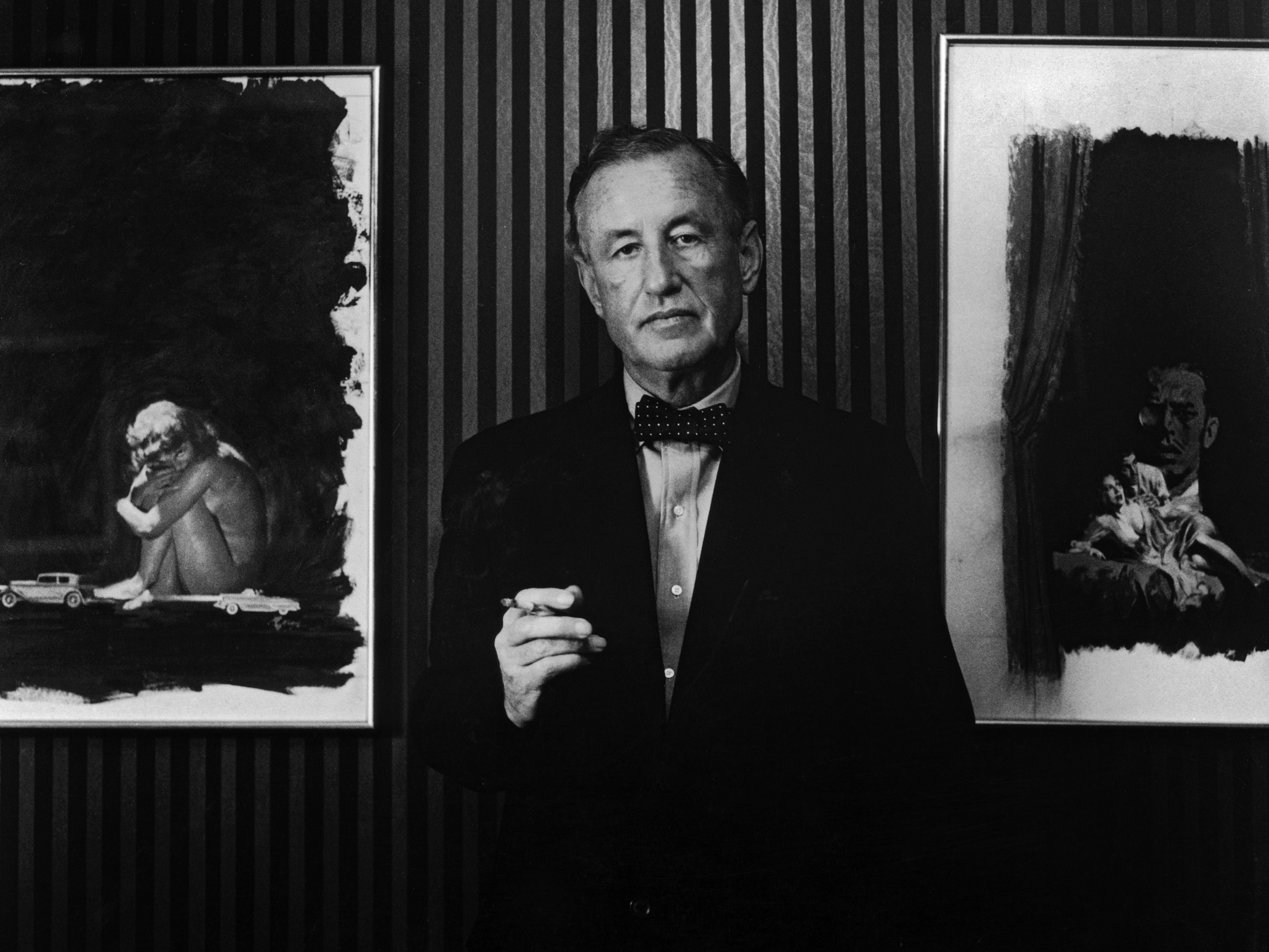 caption: British author and creator of James Bond Ian Fleming (1908-1964) with two pieces of original artwork from the American hardback editions of his books, circa 1960.