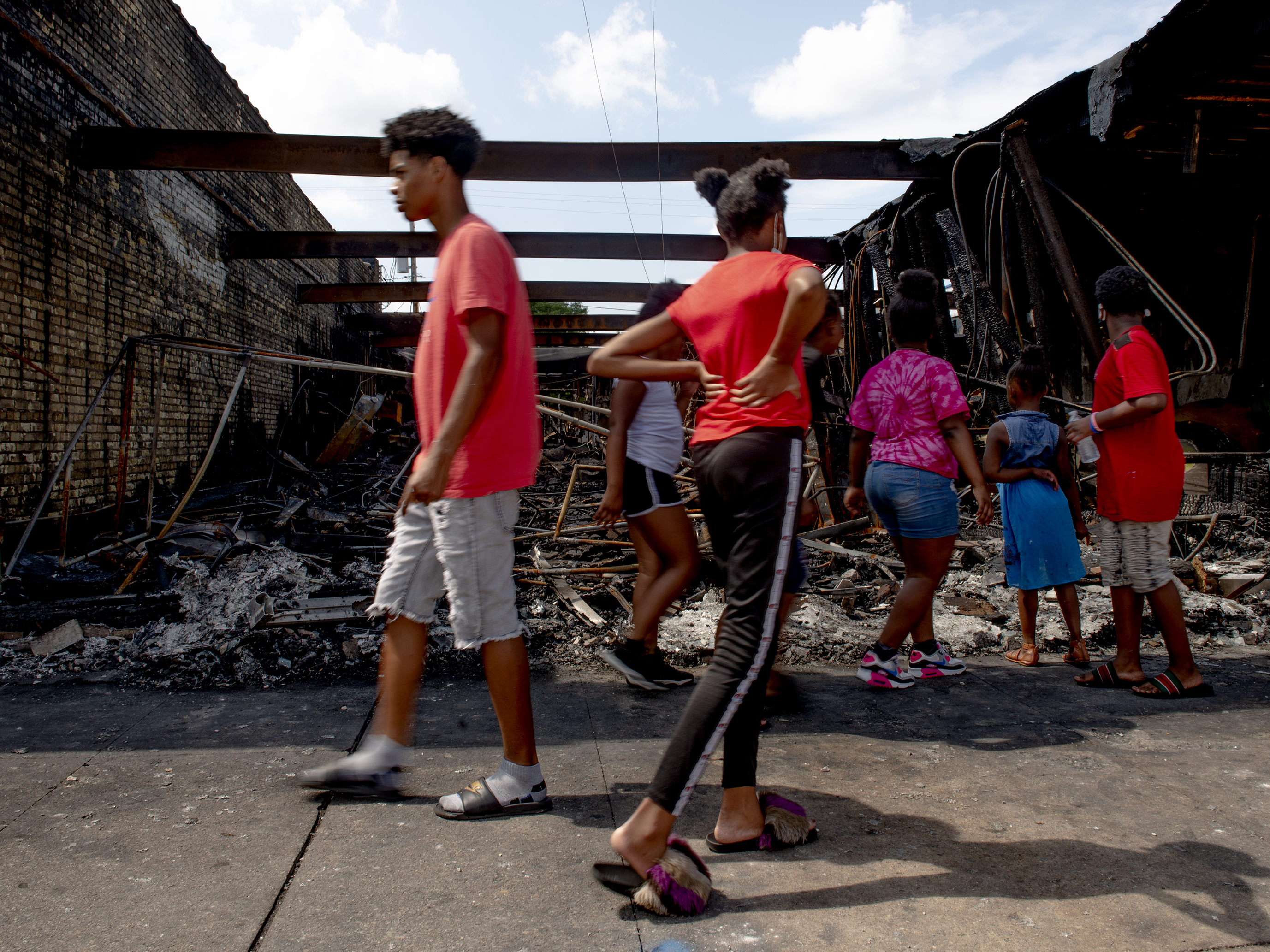 caption: People pass by a destroyed building in Kenosha, WI.