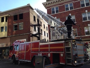 caption: A Seattle Fire truck retracts a ladder from the Hudson Building in the International District where a fire burned the upper floors of a century-old brick building.