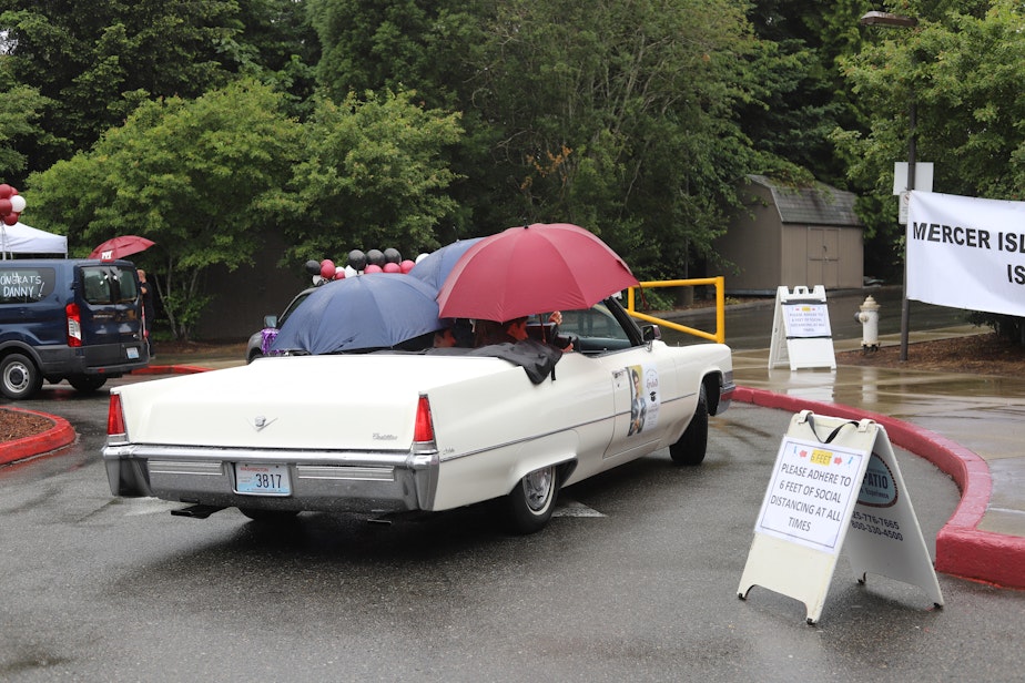 caption: A family combats the rain with umbrellas in their convertible as they watch their senior graduate on a makeshift stage at Mercer Island High School on June 9, 2020.
