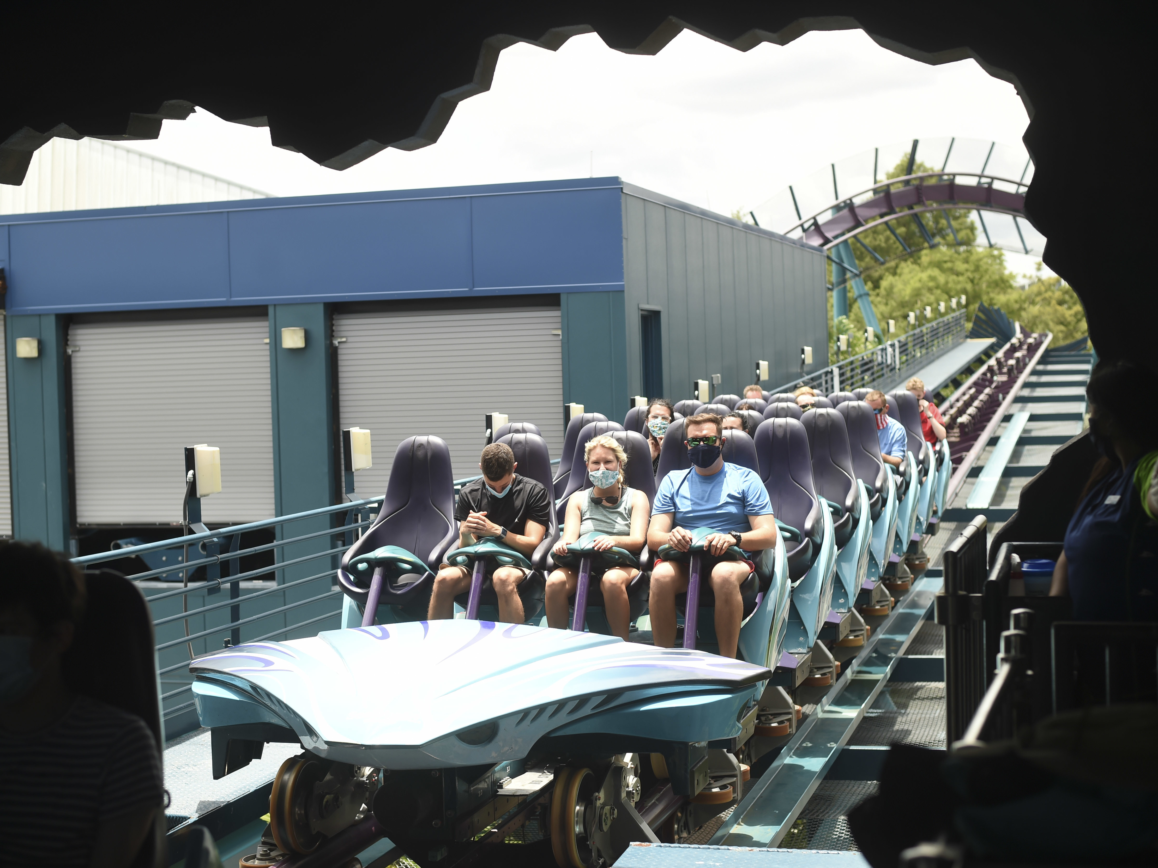 caption: Visitors wear face masks while riding a roller coaster Thursday at the SeaWorld amusement park in Orlando, Fla. SeaWorld is reopening this week after being closed due to the COVID-19 pandemic. Florida and more than 20 other states continue to see a rise in new daily cases.