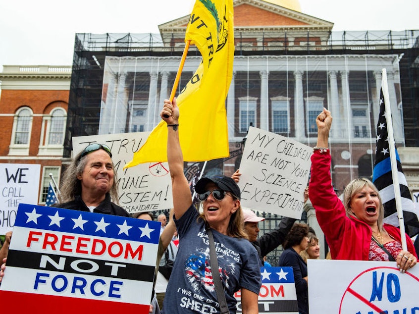 caption: Demonstrators gather outside the Massachusetts State House in Boston to protest COVID-19 vaccination and mask mandates. The political divide on the issue is only deepening, as Republican leaders of other states take more steps to thwart mandates.