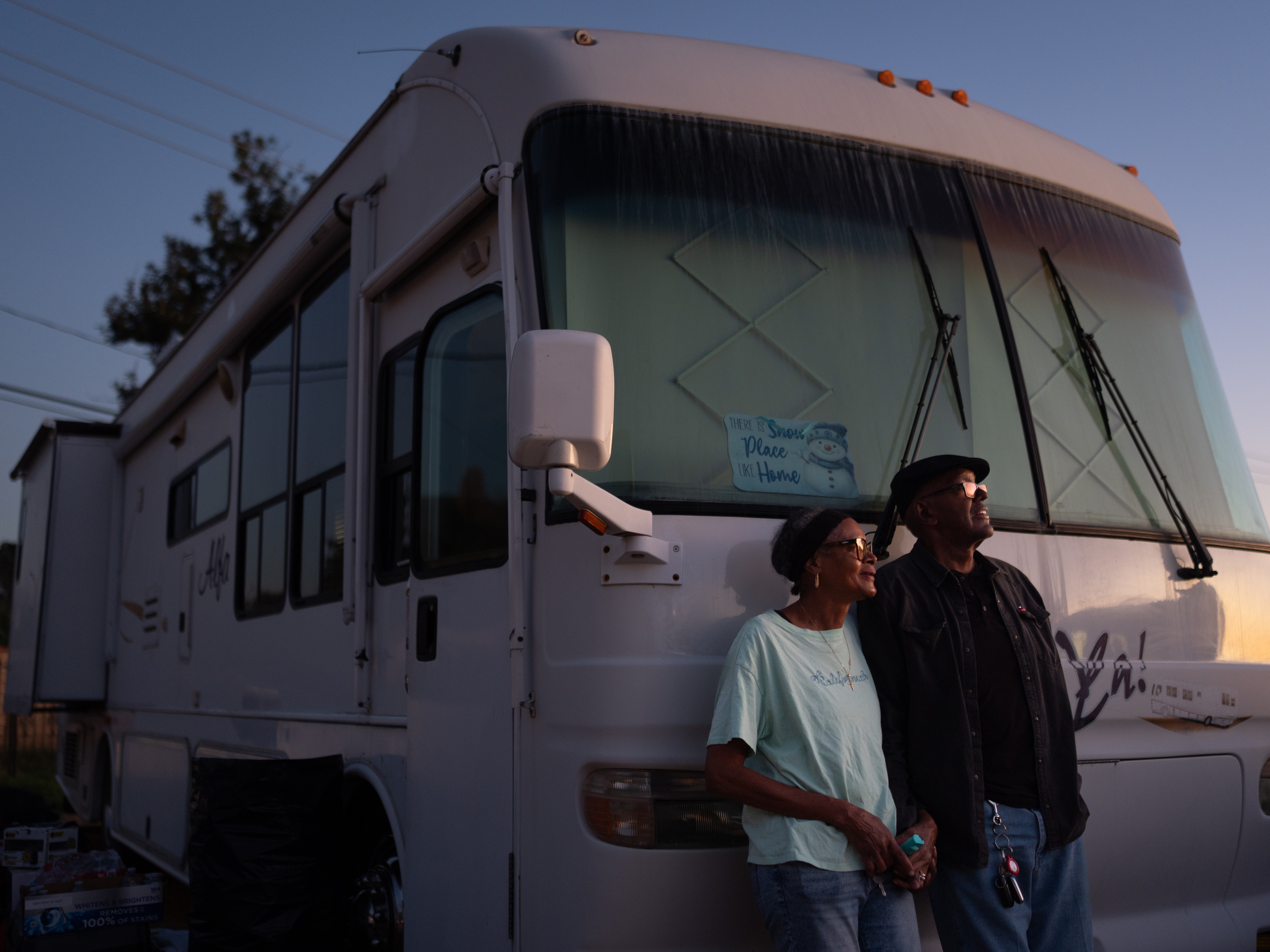 caption: Ellaird Bailey and his wife, Charlotte, who lost their home in Altadena, Calif., to a wildfire in early 2025, stand in front of their recreational vehicle in December 2025. The RV is parked on the property where their house once stood. It can take years for disaster survivors to recover, often with the help of local Federal Emergency Management Agency workers.