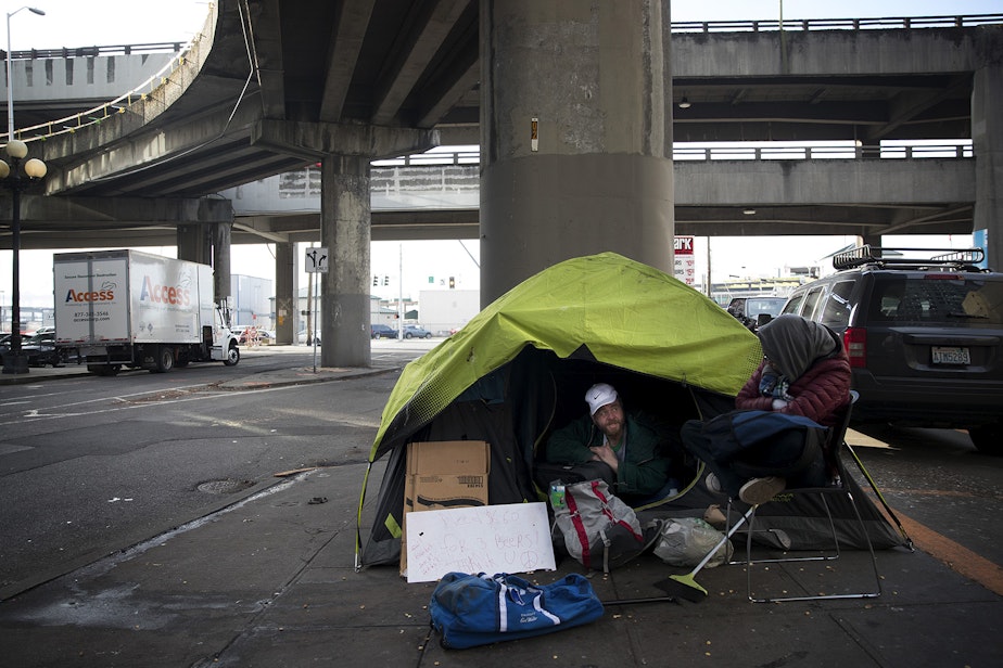 caption: Alex Shpungin talks with a friend, Dorea, right, while sitting in his tent on Tuesday, January 15, 2019, near the intersection of Columbia Street and Alaskan Way South in Seattle. Shpungin has lived at this location for 3 months and hopes to stay there as long as possible.
