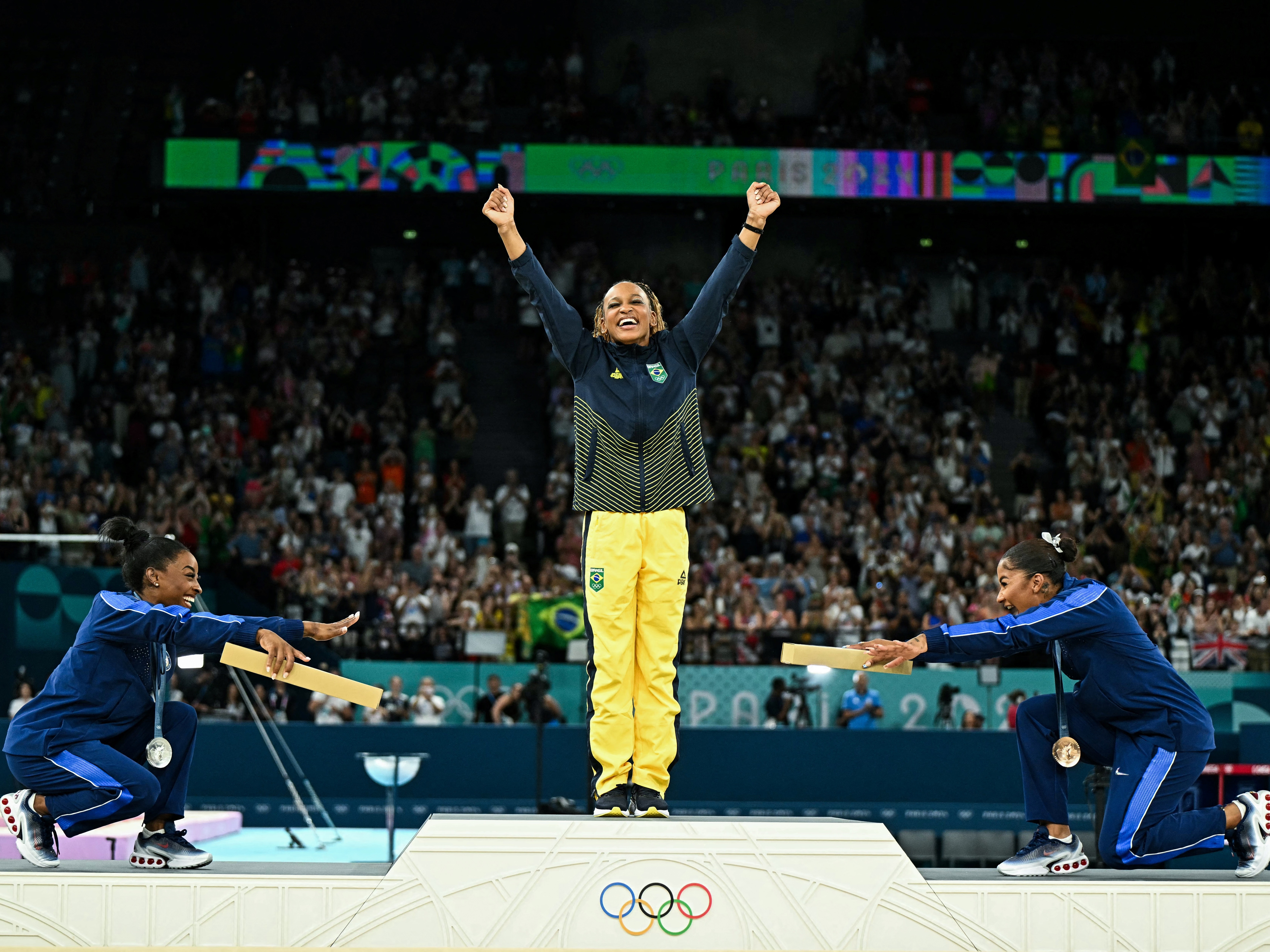 caption: Simone Biles, left, joins teammate Jordan Chiles in pointing toward gold medalist Rebeca Andrade of Brazil. Biles won silver and Chiles bronze in the women's floor exercise at the Paris 2024 Olympic Games — the first time three Black athletes have shared the podium in Olympic gymnastics.