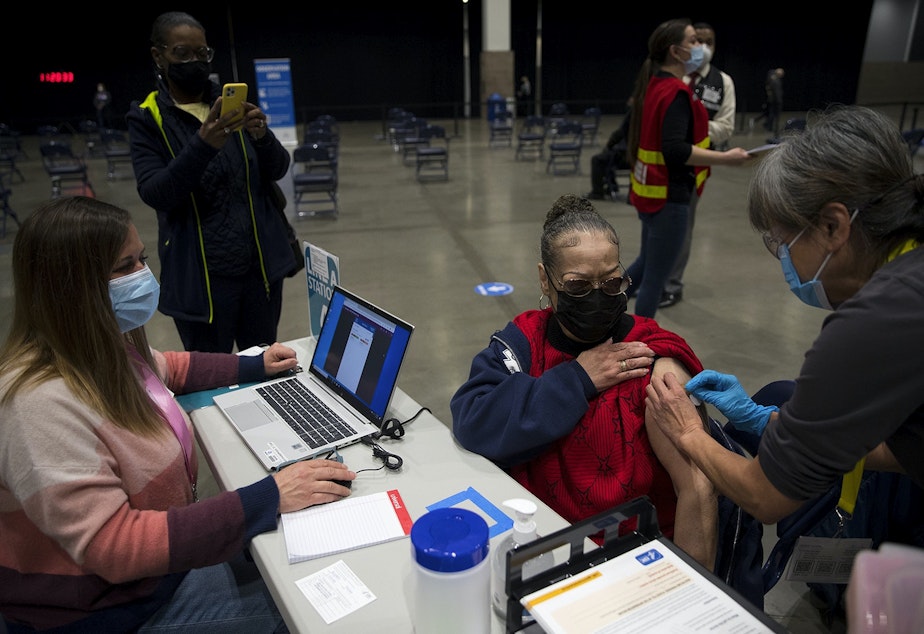 caption: Susan Hughes receives a Covid-19 vaccine at the mass vaccination site on March 13, 2021 at Seattle's Lumen Field Event Center.