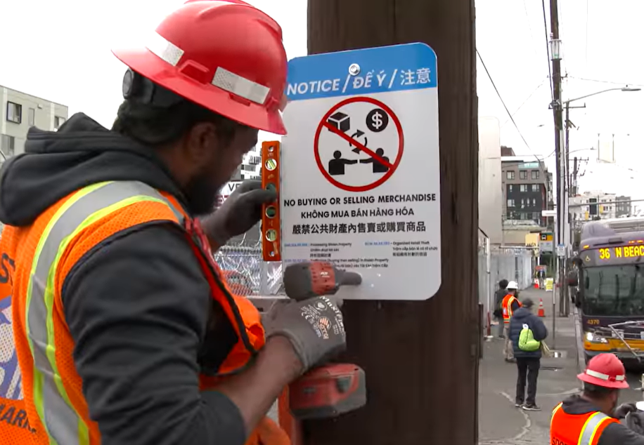 caption: An SDOT worker posts a sign in Seattle's Chinatown-International District as part of an effort by police to counter illegal street vending in the area. 