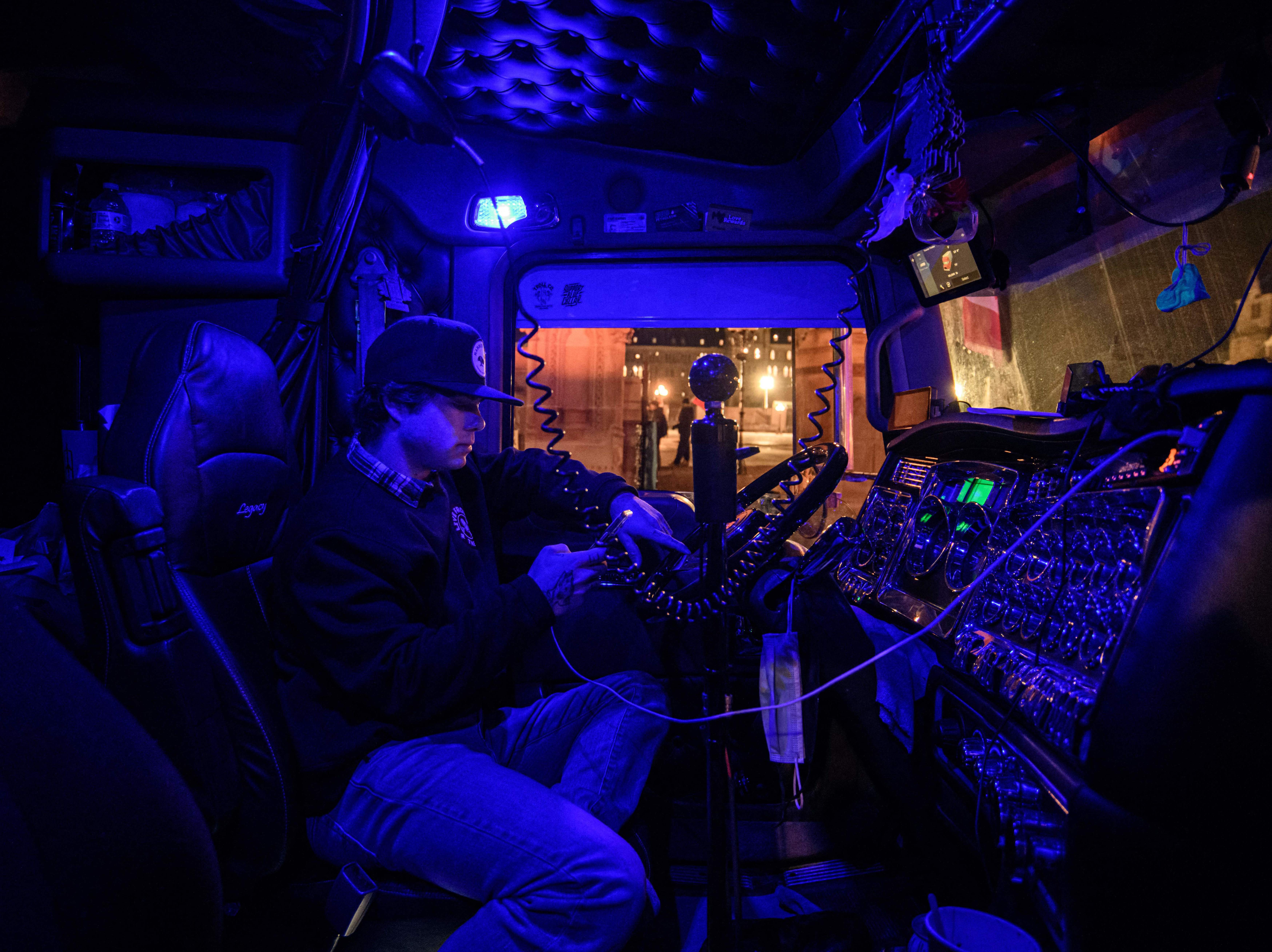 caption: A man protests as he sits in the cab of his truck in Ottawa, during a demonstration by truck drivers over pandemic health rules and the Trudeau government. Millions of dollars that were donated to boost the protests are now in limbo.