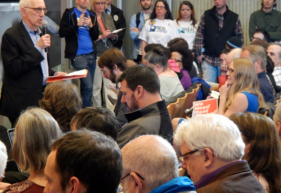 caption: Seattle City Council member Nick Licata speaks to an overflow crowd about rent control in the city council chambers.