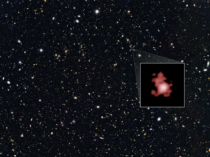 caption: This image shows a 'close-up' of the galaxy GN-z11 as imaged by the Hubble Space Telescope, superimposed on top of another image marking the galaxy's location in the sky.