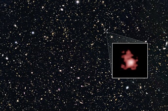 caption: This image shows a 'close-up' of the galaxy GN-z11 as imaged by the Hubble Space Telescope, superimposed on top of another image marking the galaxy's location in the sky.