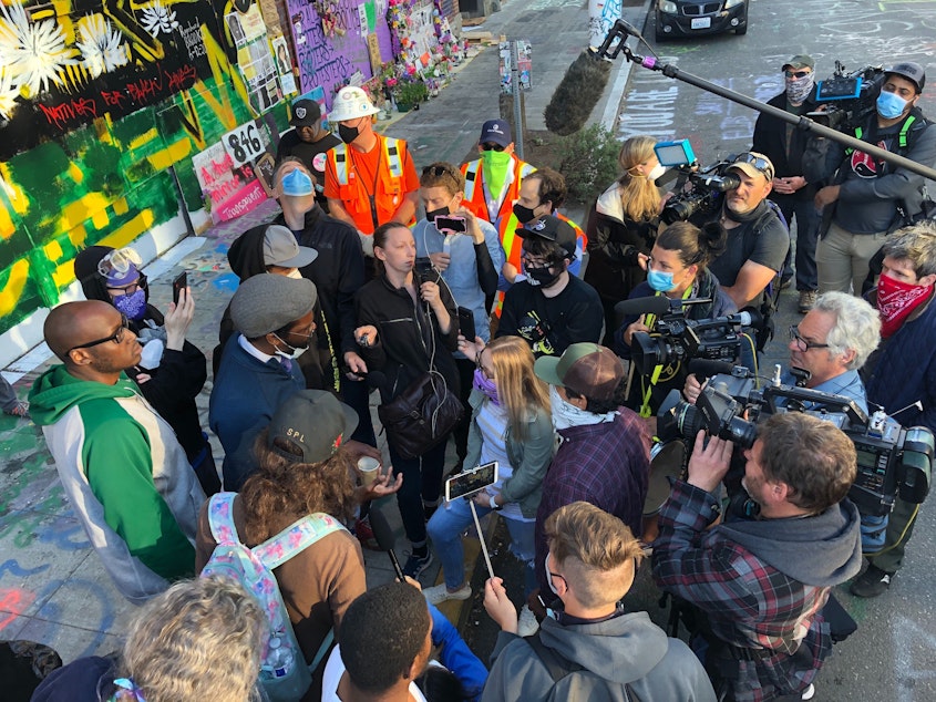 caption: Stephanie Formas from the mayor's office (center in light blue shirt and purple mask) speaks with protesters Friday morning in the CHOP while city workers were trying to remove road barriers.