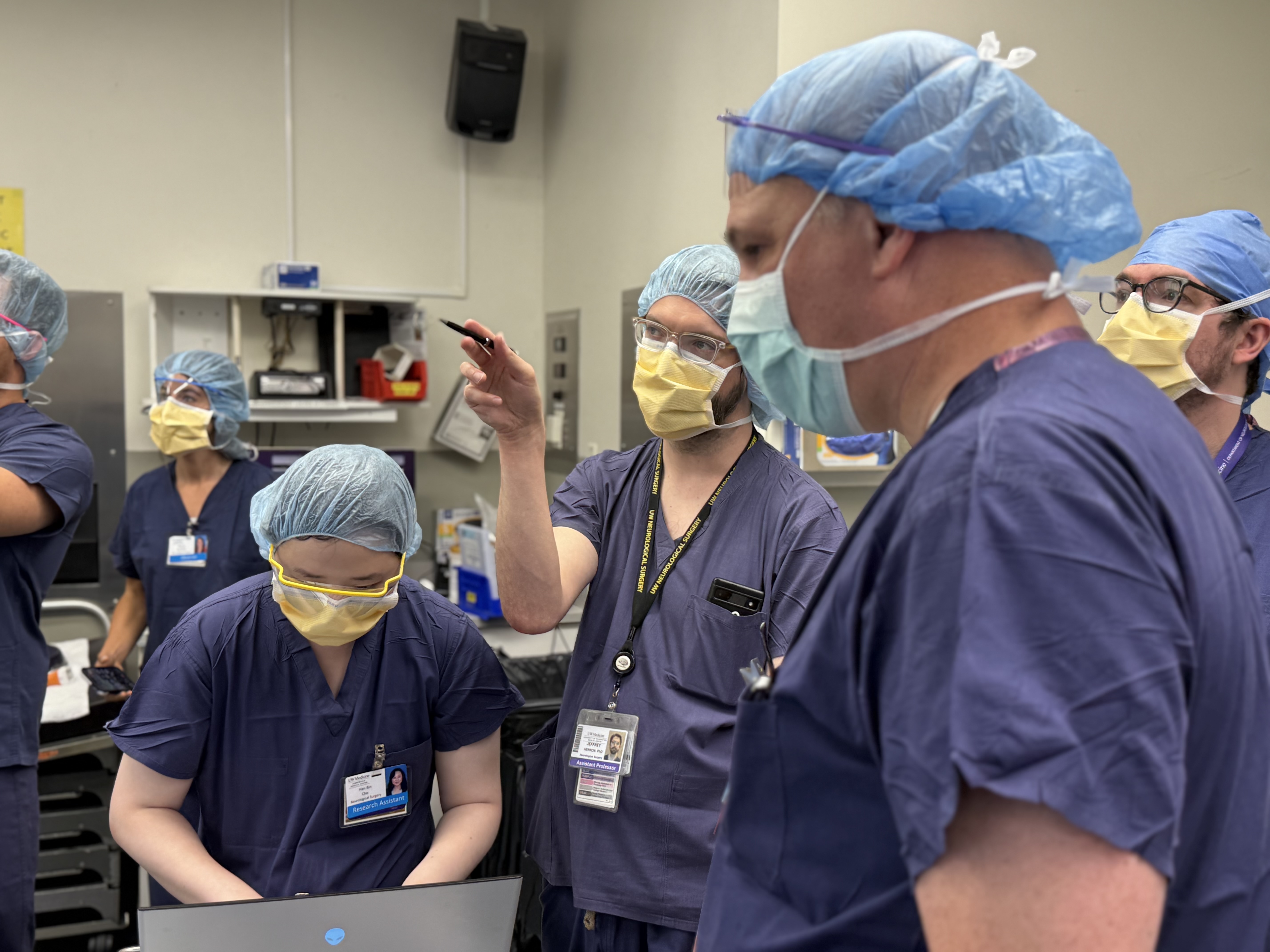 caption: Neurosurgeons and researchers during the implantation of the CorTec device into the first human patient in July at Harborview Medical Center. Doctoral student and GRIDLab researcher Hanbin Cho is shown on a laptop at the left. Dr. Jeffrey Herron is pointing with an pen in the center and Dr. Jeffrey Ojemann is in profile on the right.