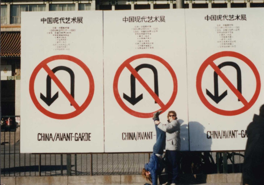 caption: Stephanie Hogan and Tim Hogan pose in front of a large sign that says “China/Avant-Garde” in Beijing, China, in February 1989.