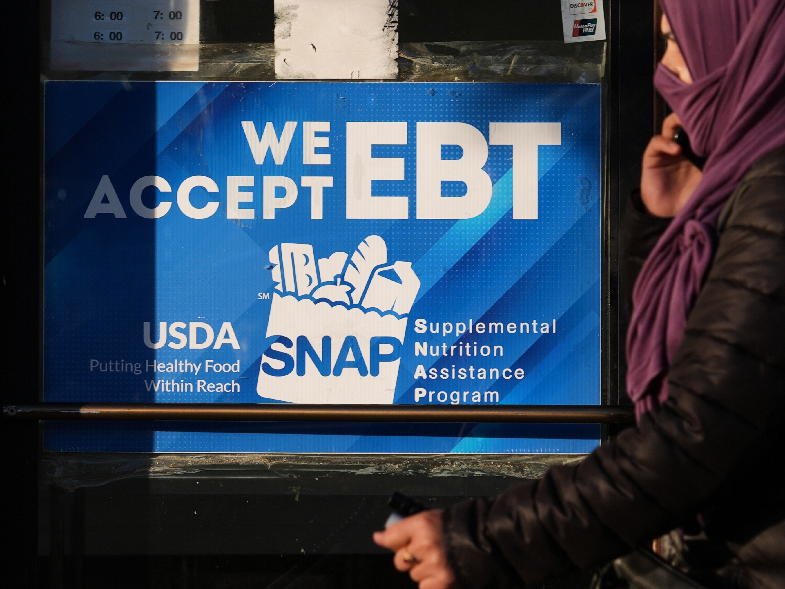 caption: A SNAP EBT information sign is displayed at a bakery as a woman walks past in Chicago, Nov. 2.