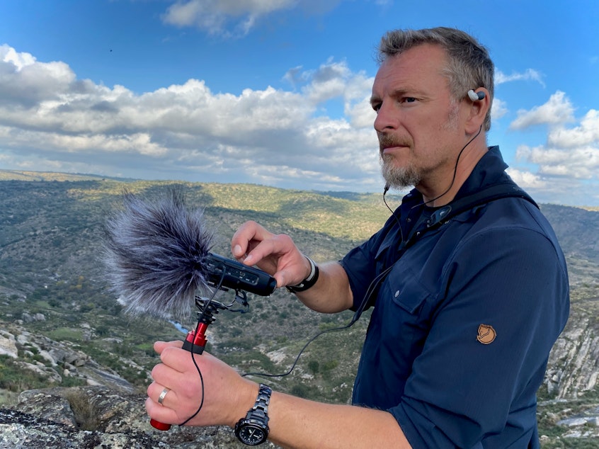 caption: Chris Morgan holds a microphone and records for THE WILD podcast in Portugal. Oct 2021. 
