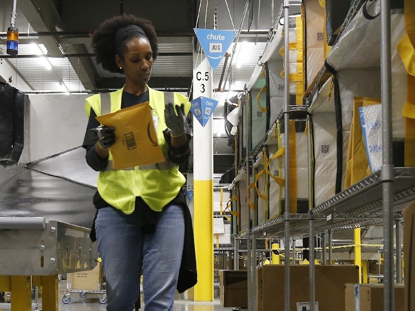 caption: An Amazon worker stows packages into special containers at a facility in Arizona. Coronavirus cases have been reported in at least 7 Amazon facilities.