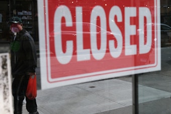 caption: A store in New York City stands closed on April 21, 2020. A year after the coronavirus pandemic was declared, millions of Americans are still unemployed.
