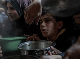 caption: A Palestinian boy waits with his pot among a crowd in Beit Lahia, in northern Gaza, while trying to get a small amount of soup from one of the few soup kitchens, on Feb. 26.