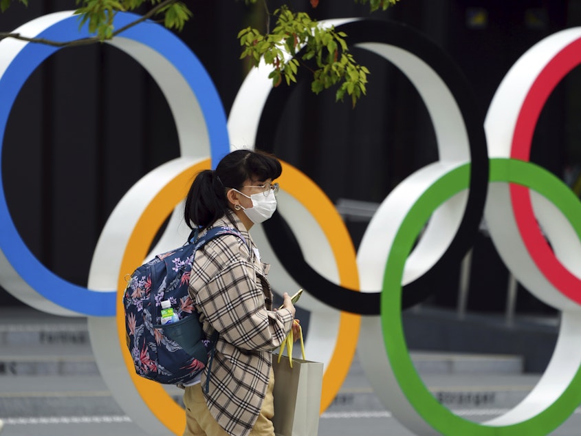 caption: A woman wearing a protective mask to help curb the spread of the coronavirus walks in front of he Olympic Rings on Tuesday in Tokyo. North Korea says it will not attend the games over COVID-19 fears.
