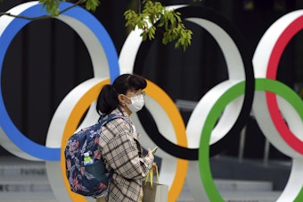 caption: A woman wearing a protective mask to help curb the spread of the coronavirus walks in front of he Olympic Rings on Tuesday in Tokyo. North Korea says it will not attend the games over COVID-19 fears.