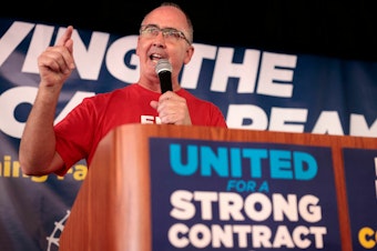 caption: UAW President Shawn Fain speaks as UAW members and their supporters gather for Solidarity Sunday at the UAW Region 1 office in Warren, Mich., on Aug. 20. The UAW has started an unprecedented strike against all three big automakers.