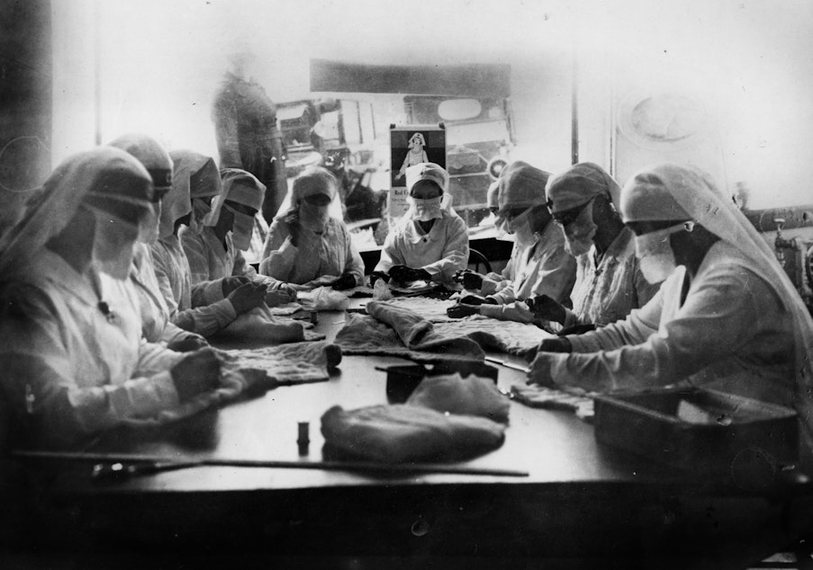 caption: December 1918. Combating influenza in Seattle, Washington, at work in the Red Cross rooms in Seattle, Washington with influenza masks on faces.