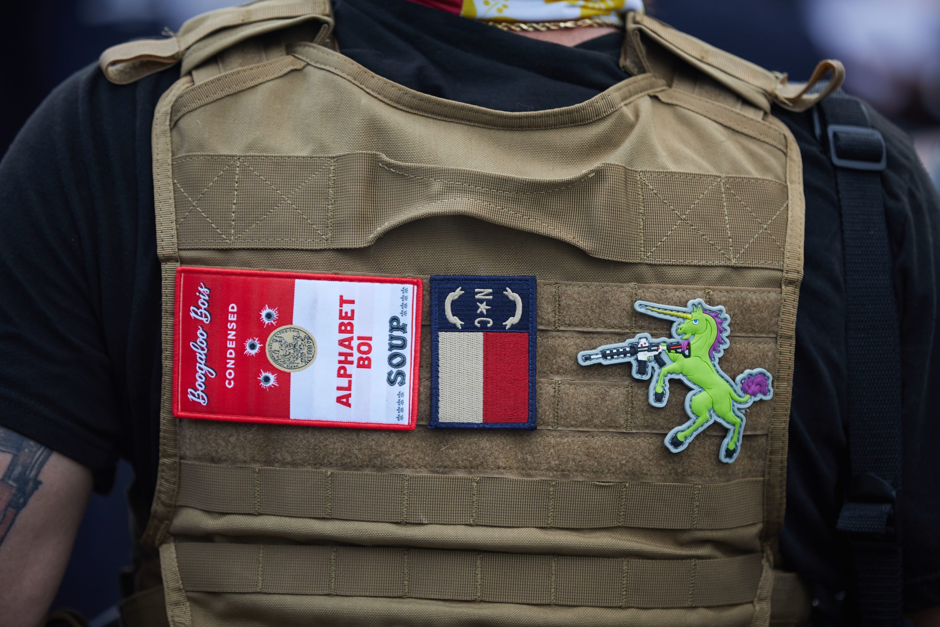 caption: A member of the far-right militia, Boogaloo Bois, walks next to protestors demonstrating outside Charlotte Mecklenburg Police Department Metro Division 2 just outside of downtown Charlotte, North Carolina, on May 29, 2020. (Logan Cyrus/AFP via Getty Images)