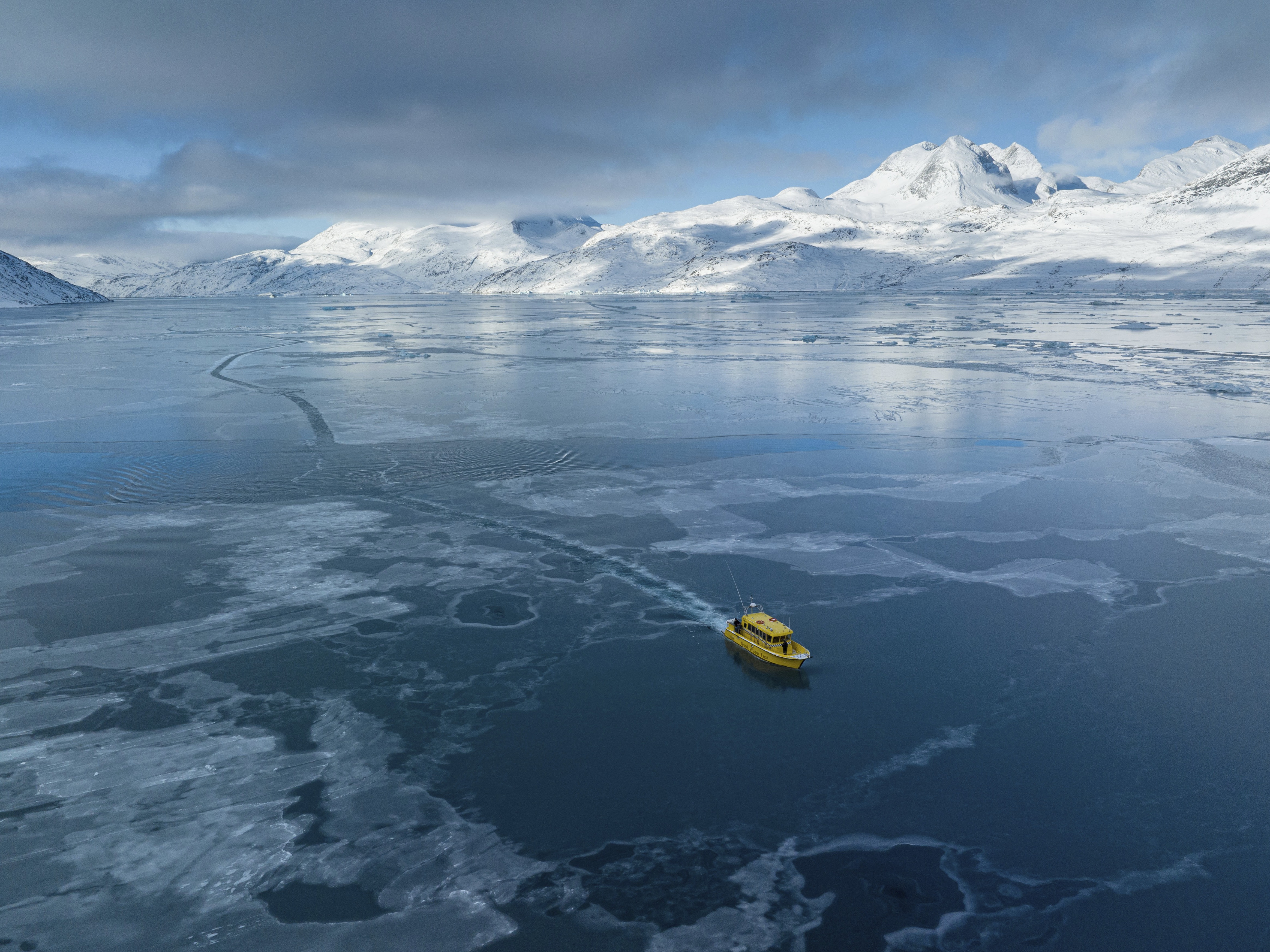 caption: A boat rides through a frozen sea inlet outside of Nuuk, Greenland on March 6.