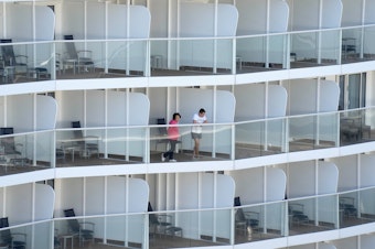 caption: Passengers look out from the Spectrum of the Seas cruise ship docked in Hong Kong on Wednesday. Thousands of passengers were being held on the ship for coronavirus testing after health authorities said nine passengers were linked to a recent omicron cluster and ordered the ship to turn back.