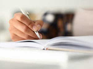 A close-up of a woman's hand writing in a notebook.