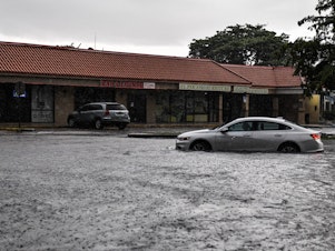 caption: A woman drives through floodwater during heavy rainfall in Miami. A new study predicts that high tide flooding in coastal areas could increase in frequency because of climate change and the lunar cycle in the mid-2030s.