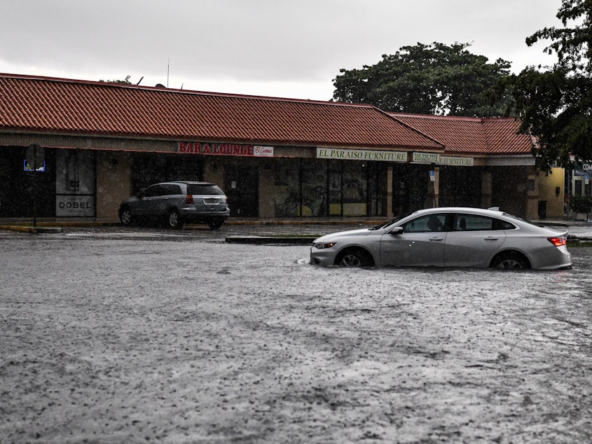 caption: A woman drives through floodwater during heavy rainfall in Miami. A new study predicts that high tide flooding in coastal areas could increase in frequency because of climate change and the lunar cycle in the mid-2030s.