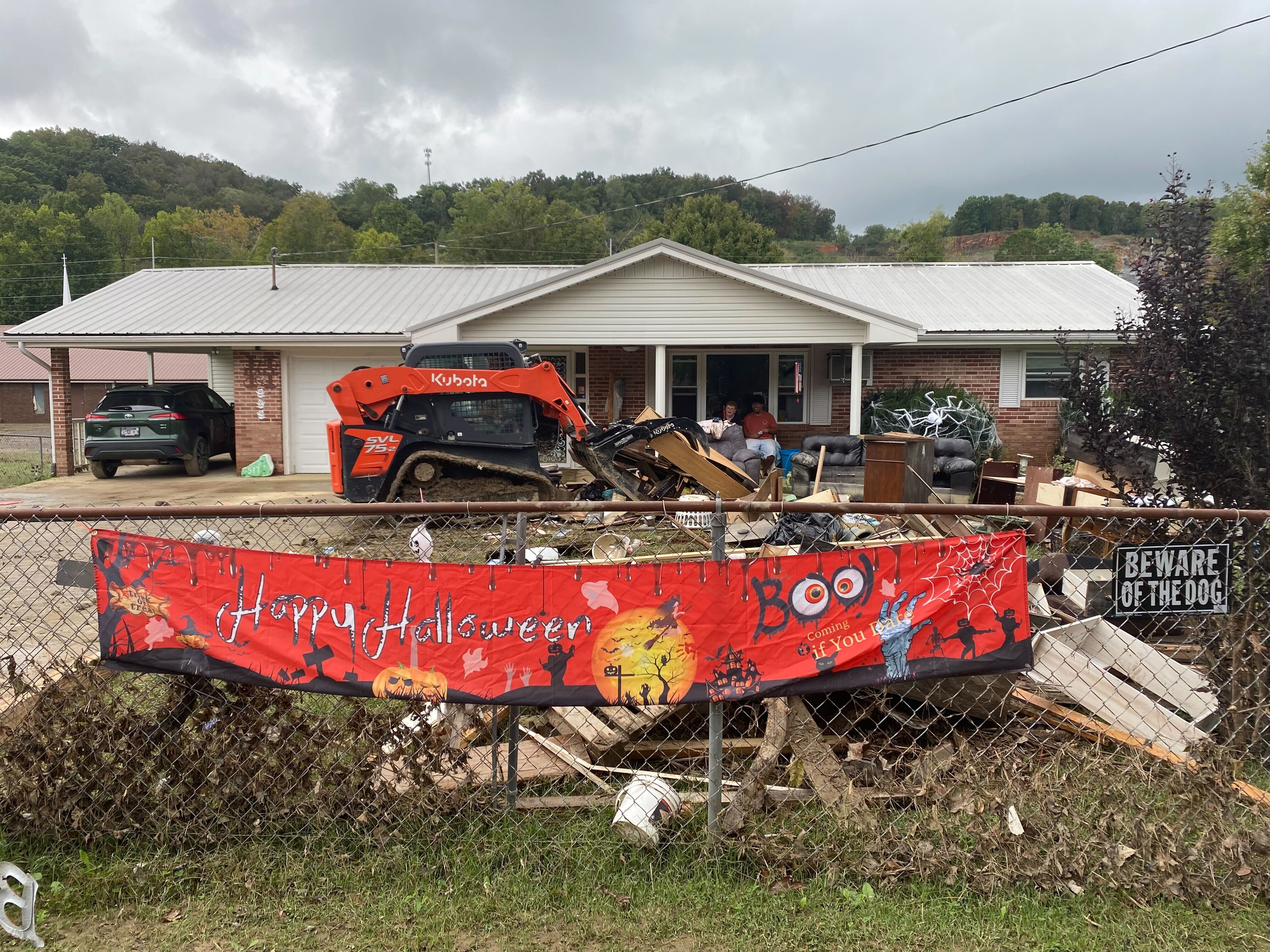 caption: Trudy Hall’s house flooded after Hurricane Helene. She sits on the porch watching as all her belongings are loaded up by volunteers, to be taken to the dump.