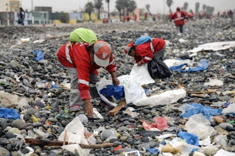 caption: Volunteers clean up plastic waste on a beach in Peru.